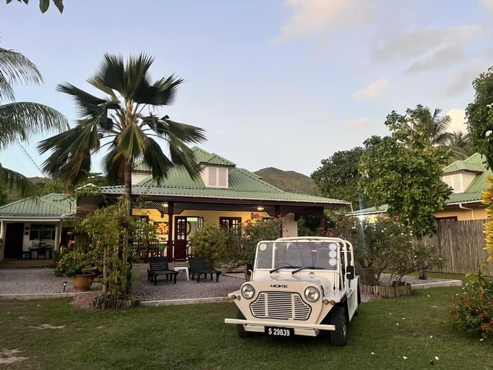 Akşam ışığında yeşil çatılı bir Kreol pansiyonun çimeninde krem rengi modern Mini Moke