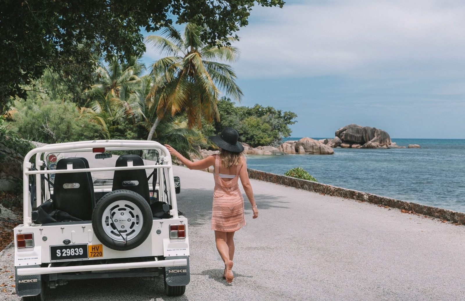 Arkadan görülen beyaz modern Mini Moke, bagaj kapağında stepne, granit kayalı kıyı yolunda ve ötesinde deniz